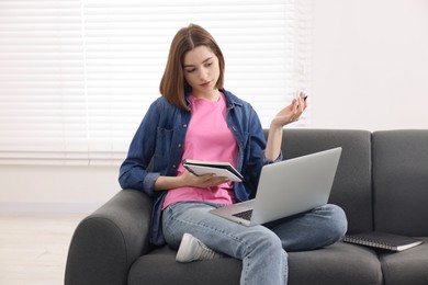 Teenager taking notes while working with laptop at home. Remote job