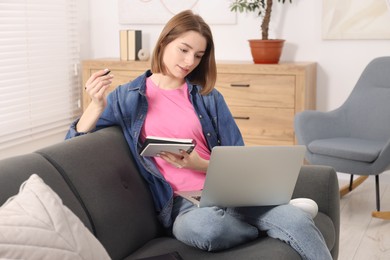 Teenager taking notes while working with laptop at home. Remote job