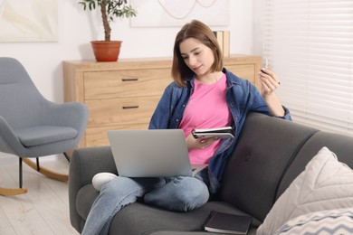 Photo of Teenager taking notes while working with laptop at home. Remote job