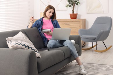 Teenager taking notes while working with laptop at home. Remote job