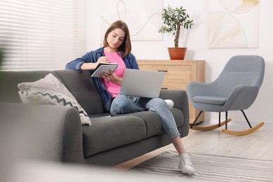 Photo of Teenager taking notes while working with laptop at home. Remote job