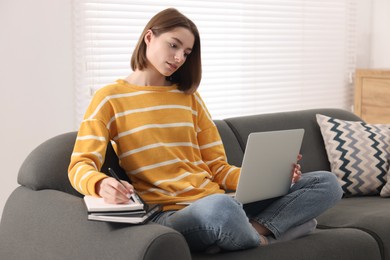 Teenager taking notes while working with laptop at home. Remote job