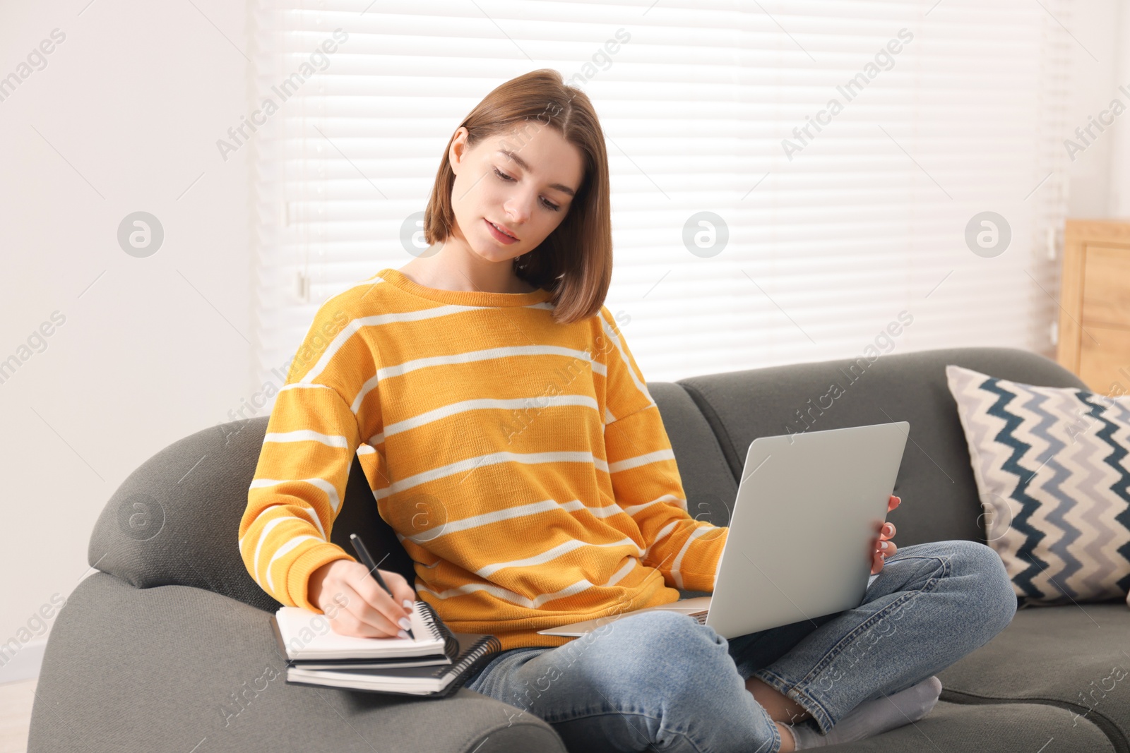 Photo of Teenager taking notes while working with laptop at home. Remote job