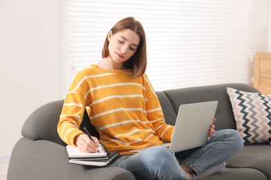 Teenager taking notes while working with laptop at home. Remote job