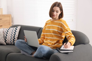 Teenager taking notes while working with laptop at home. Remote job