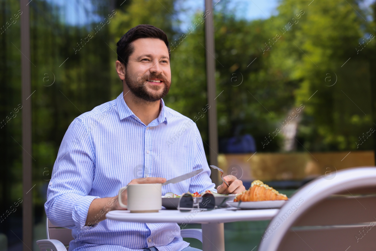 Photo of Happy man having breakfast in outdoor cafe, space for text