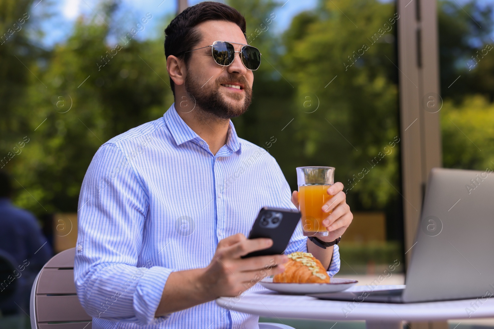 Photo of Happy man using smartphone during breakfast in outdoor cafe