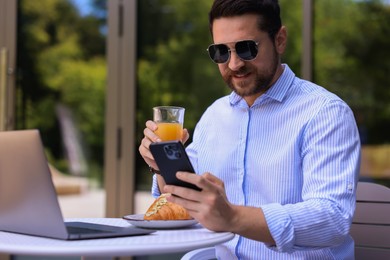 Happy man using smartphone during breakfast in outdoor cafe