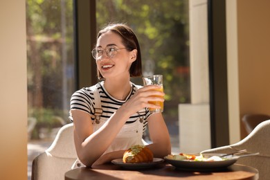 Photo of Happy woman having tasty breakfast in cafe, space for text