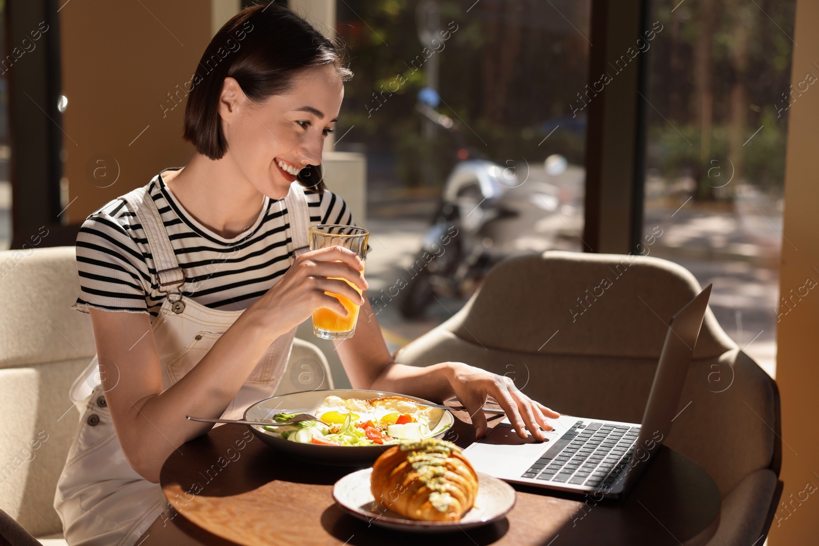 Photo of Happy woman having tasty breakfast and using laptop in cafe