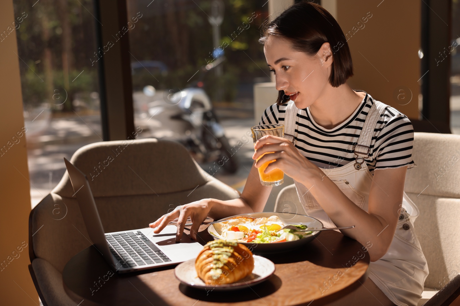 Photo of Woman having tasty breakfast and using laptop in cafe