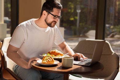 Photo of Happy man having tasty breakfast and using laptop in cafe