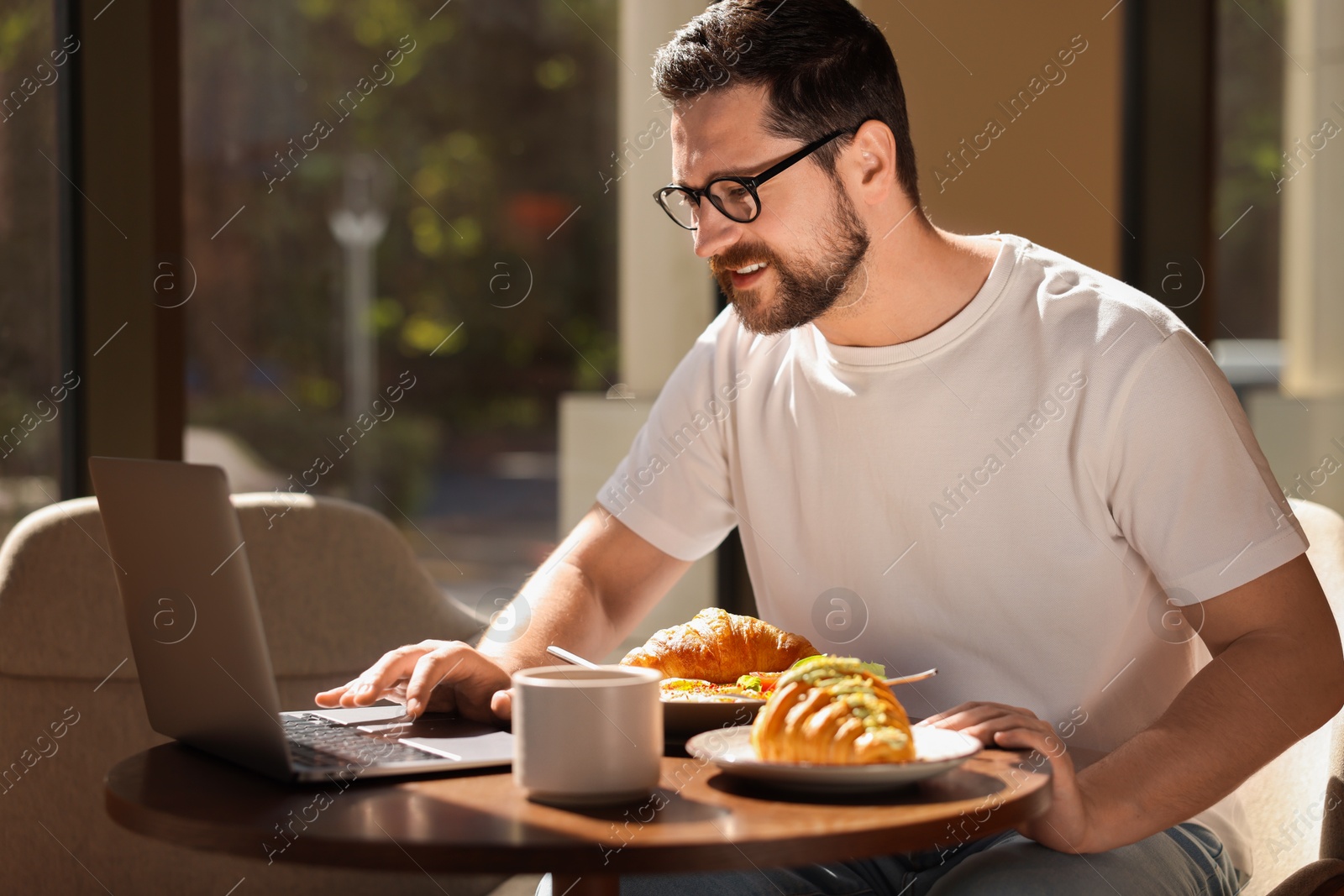 Photo of Happy man having tasty breakfast and using laptop in cafe