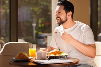 Happy man having tasty breakfast in cafe