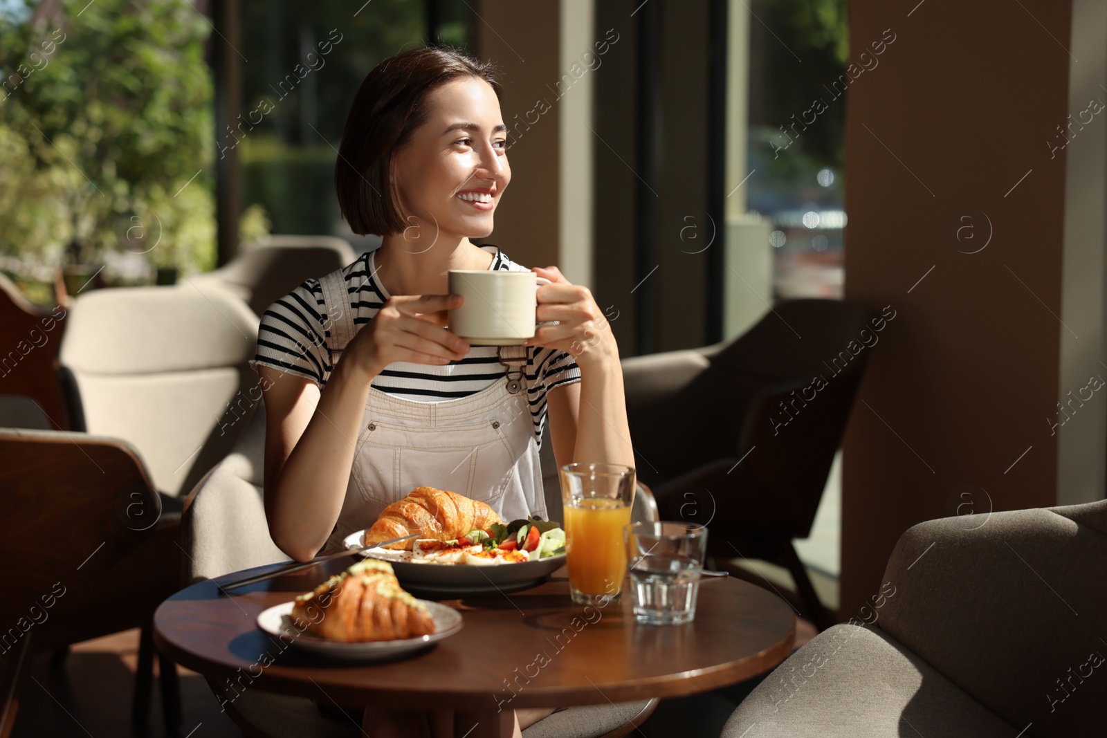 Photo of Happy woman having tasty breakfast in cafe, space for text