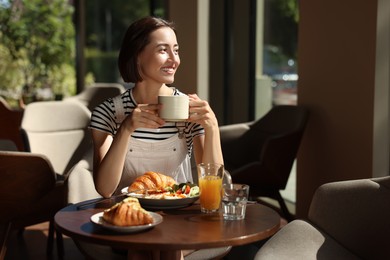 Happy woman having tasty breakfast in cafe, space for text