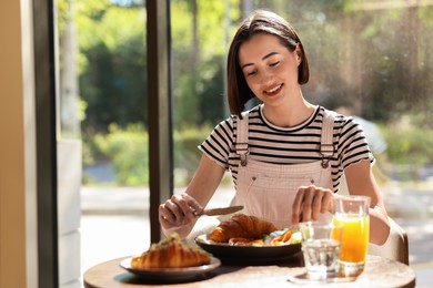 Happy woman having tasty breakfast in cafe, space for text