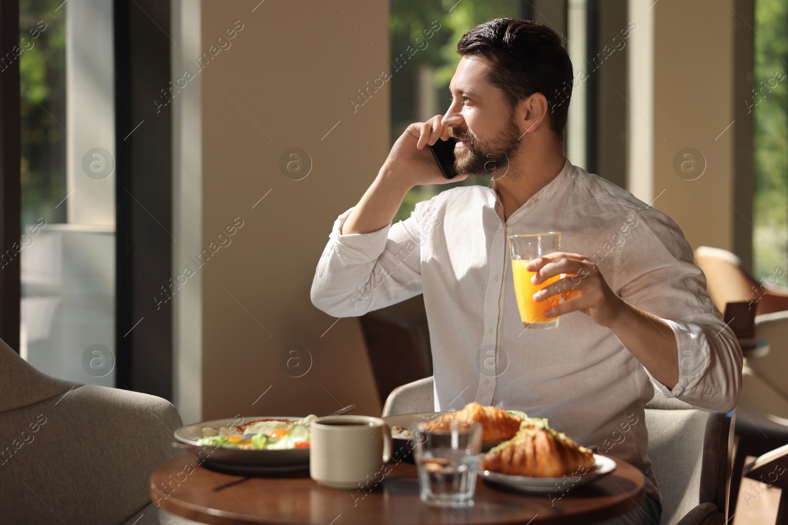 Photo of Happy man having tasty breakfast while talking on smartphone in cafe, space for text