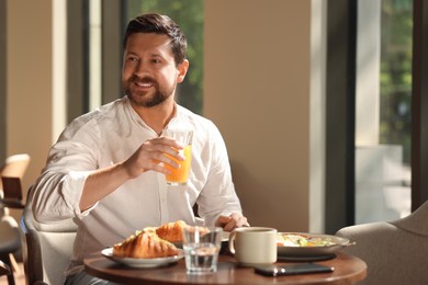 Happy man having tasty breakfast in cafe, space for text