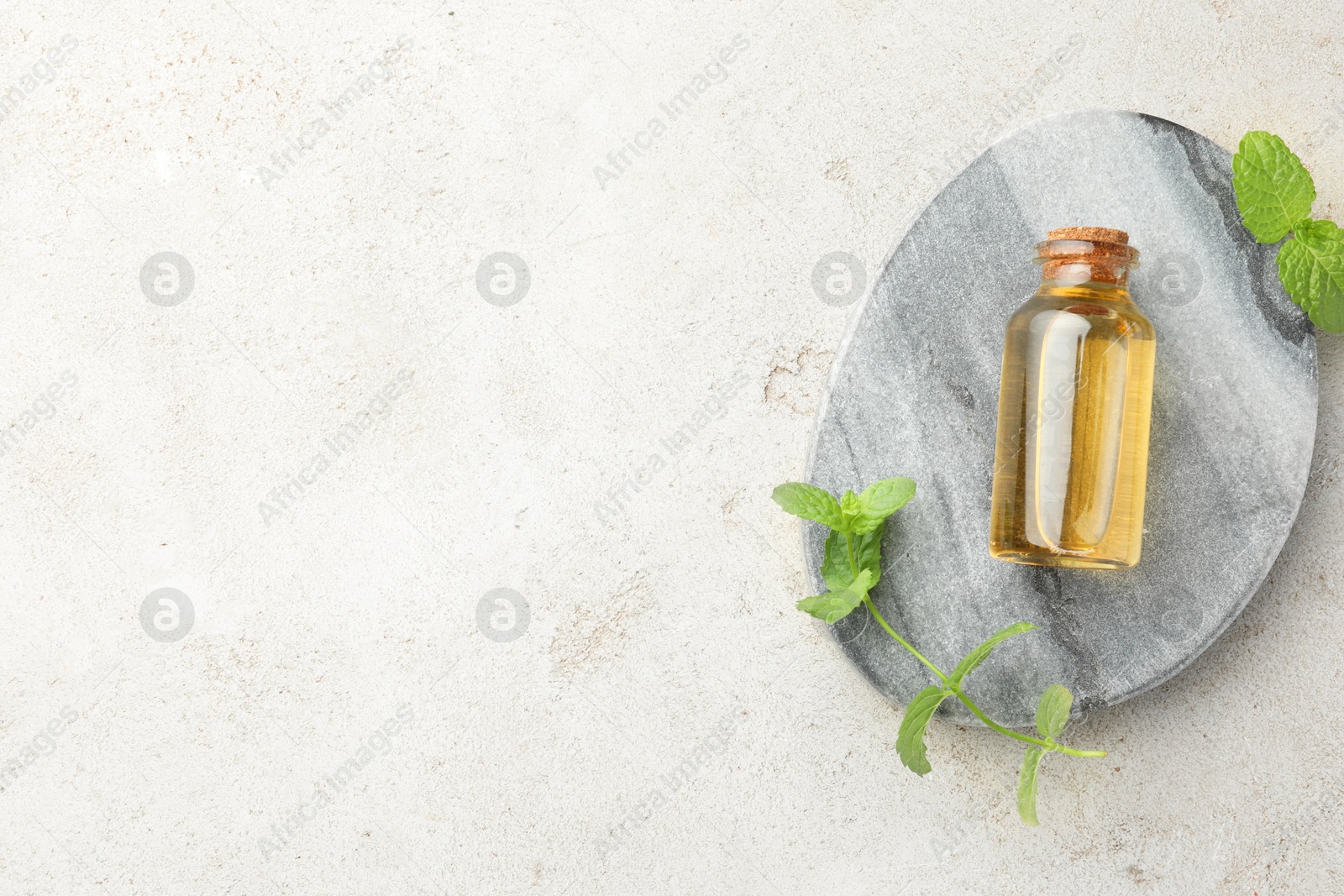 Photo of Bottle of essential oil and mint on light textured table, top view. Space for text