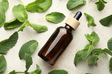 Bottle of essential oil and mint on light textured table, flat lay