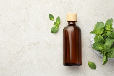 Photo of Bottle of essential oil and mint on light textured table, flat lay. Space for text