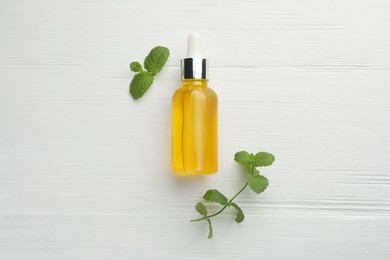 Bottle of essential oil and mint on white wooden table, flat lay