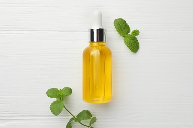 Bottle of essential oil and mint on white wooden table, flat lay