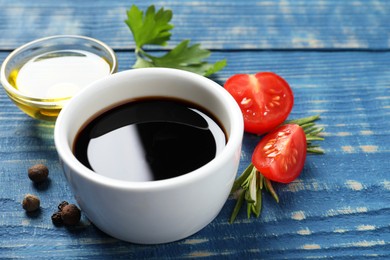 Balsamic vinegar, tomatoes, peppercorns and herbs on blue wooden table, closeup