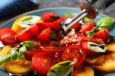 Photo of Pouring balsamic vinegar onto tasty salad on table, closeup