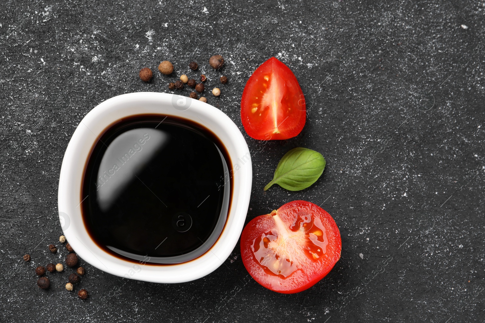 Photo of Balsamic vinegar, tomato and other products on black textured table, flat lay. Space for text