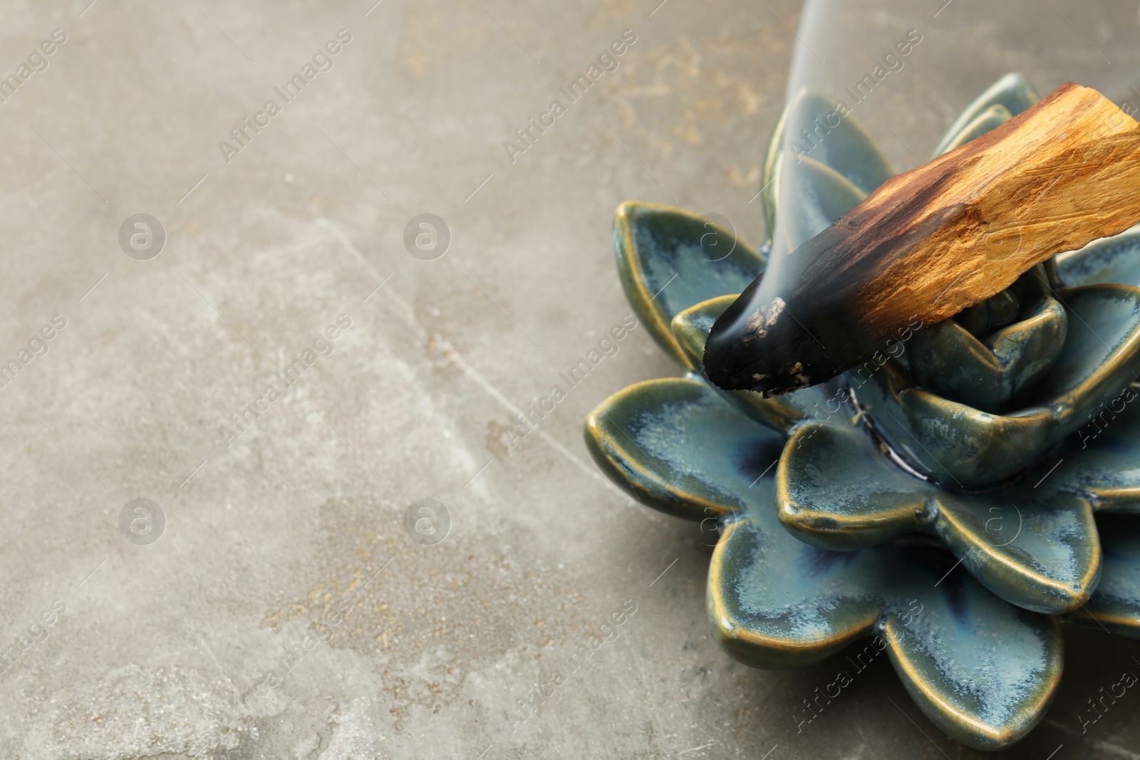 Photo of Smoldering Palo Santo stick and ceramic succulent on gray textured table, closeup. Space for text