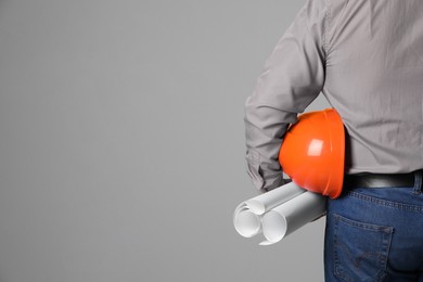 Engineer with hard hat and drafts on grey background, closeup. Space for text