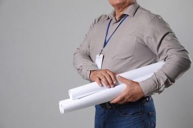 Engineer with plastic badge and drafts on grey background, closeup. Space for text