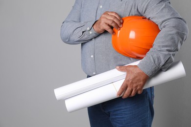 Engineer with hard hat and drafts on grey background, closeup. Space for text