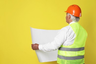 Engineer in hard hat with draft on yellow background, space for text