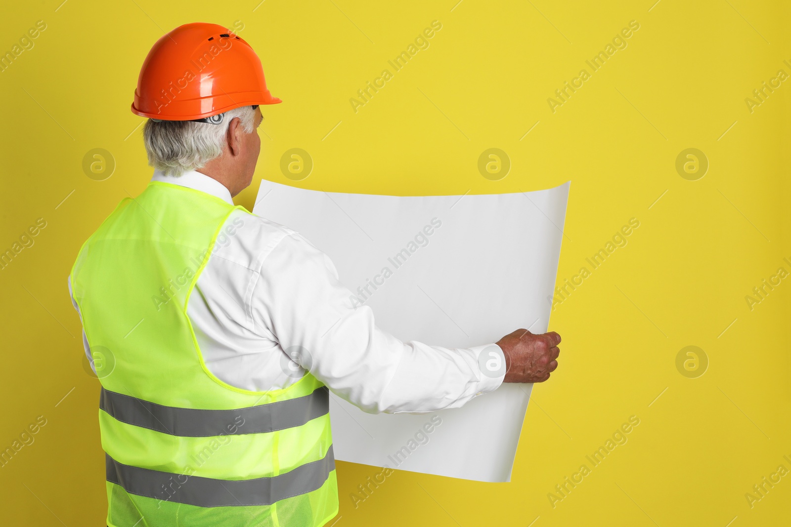 Photo of Engineer in hard hat with draft on yellow background, space for text