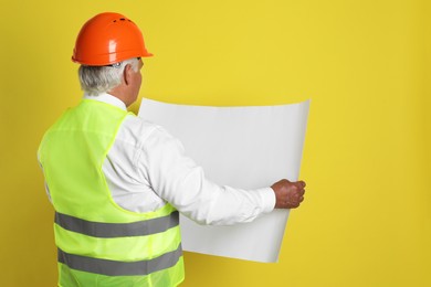 Engineer in hard hat with draft on yellow background, space for text