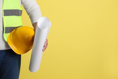 Engineer with hard hat and draft on yellow background, closeup. Space for text