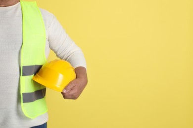 Engineer with hard hat on yellow background, closeup. Space for text