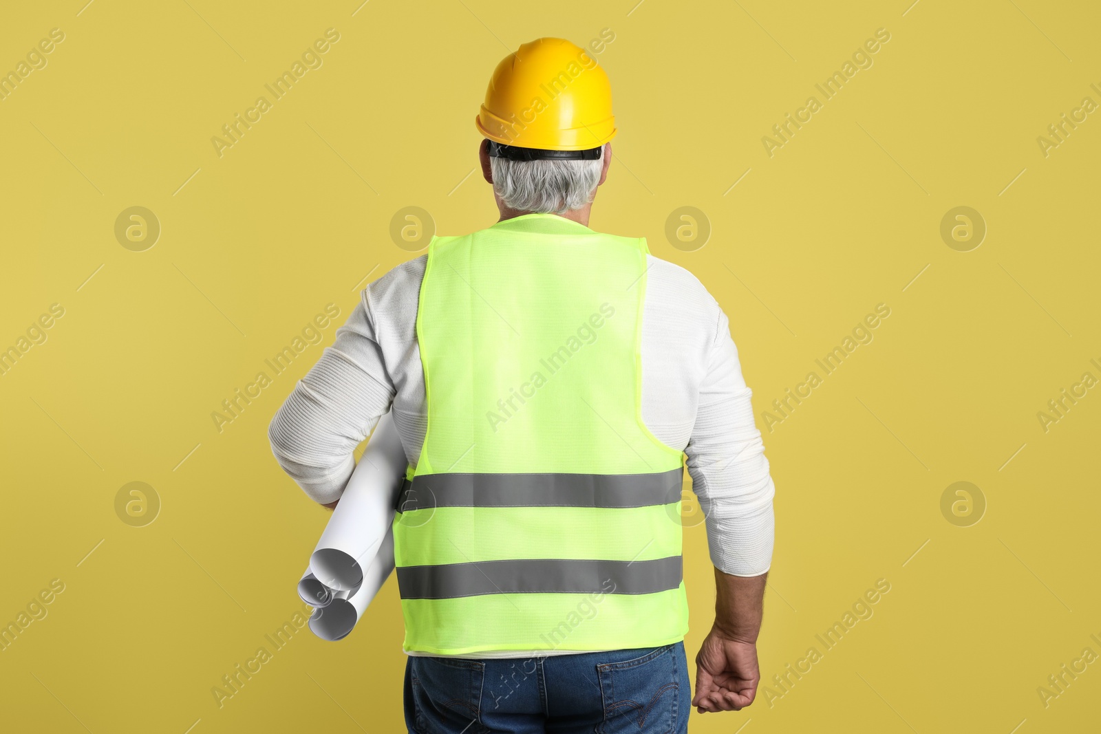 Photo of Engineer in hard hat with drafts on yellow background, back view