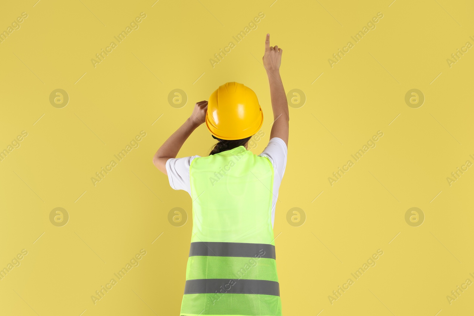 Photo of Engineer in hard hat pointing at something on yellow background, back view