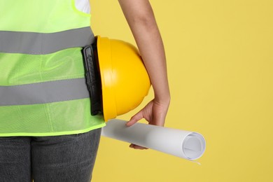 Engineer with hard hat and draft on yellow background, closeup. Space for text