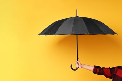 Man holding black umbrella on yellow background, closeup