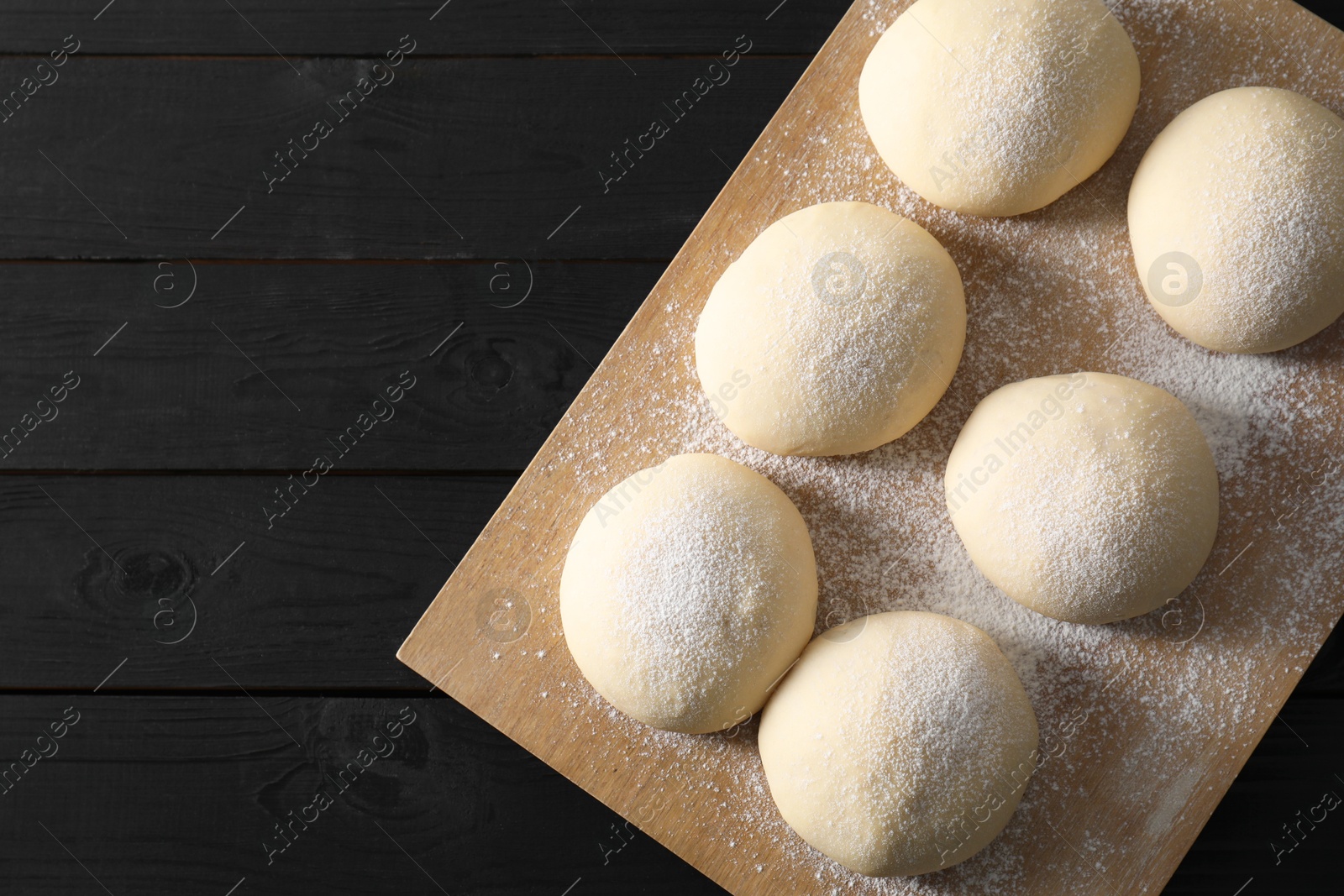 Photo of Raw dough balls on black wooden table, top view. Space for text