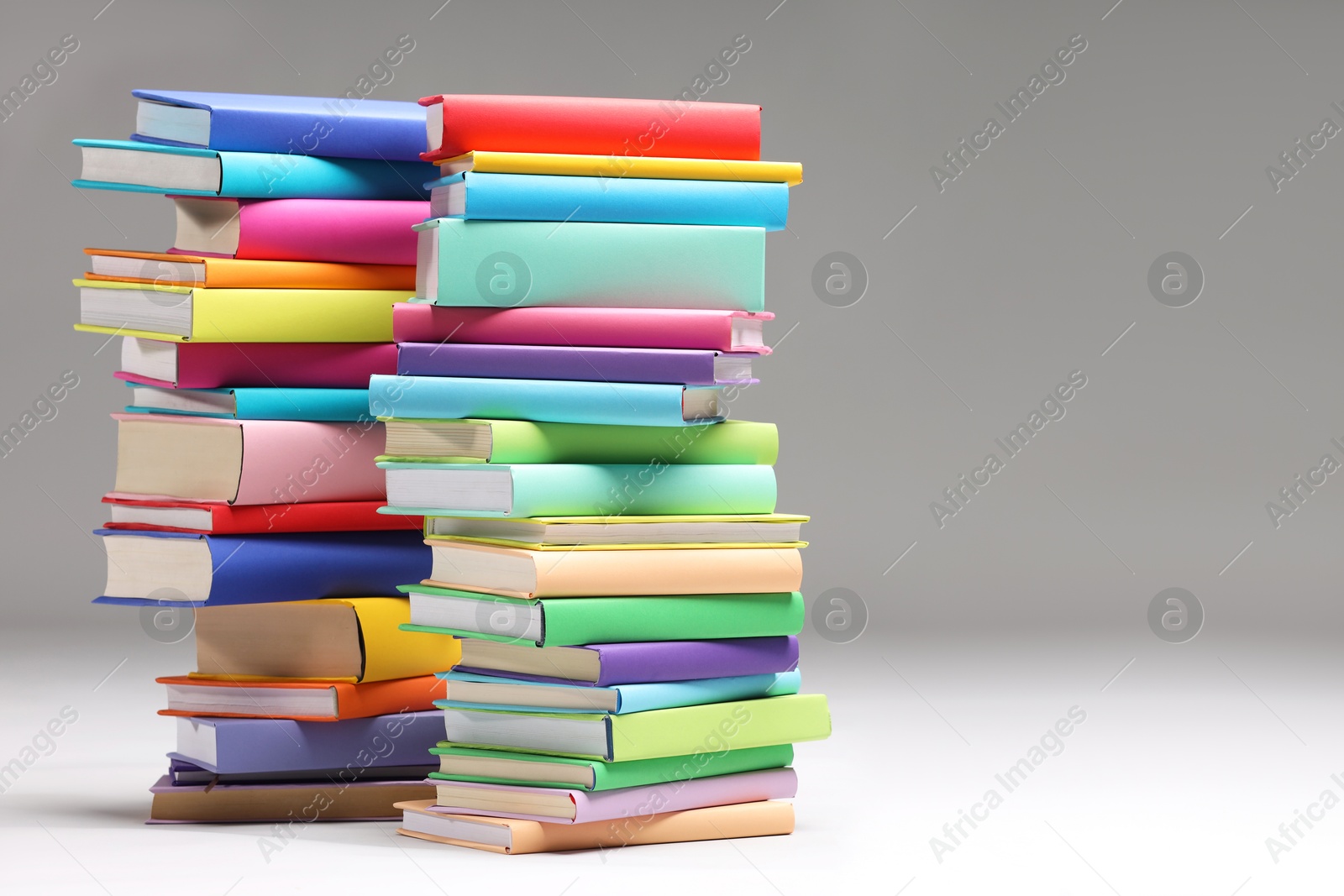 Photo of Stacks of colorful books on light grey background, space for text