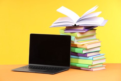 Photo of Stack of colorful books and laptop on yellow background