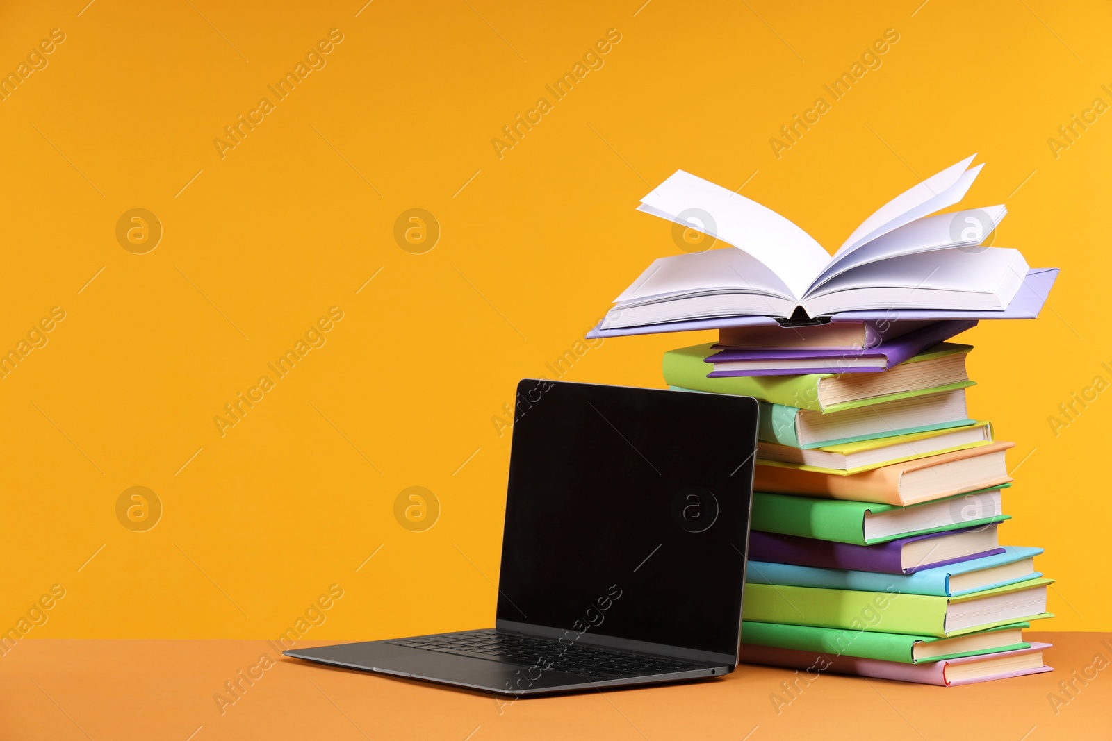 Photo of Stack of colorful books and laptop on orange background, space for text