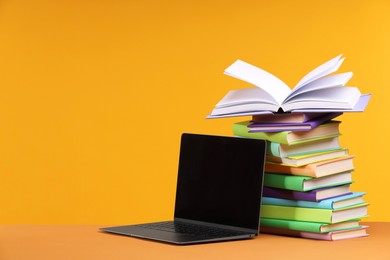 Stack of colorful books and laptop on orange background, space for text