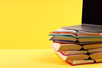 Photo of Stack of colorful books and laptop on yellow background, space for text